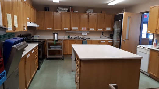 Photo of Kitchen showing large work island, commercial fridge, triple sinks and 2 stoves.