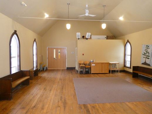 Historic sanctuary showing open floor area with carpet on the centre of the floor and old church pews placed along the walls.